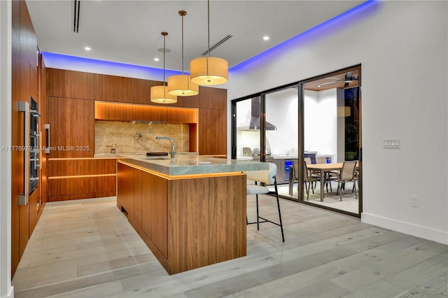 kitchen with modern cabinets, tasteful backsplash, light wood-type flooring, a sink, and brown cabinets