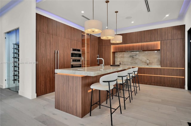 kitchen with modern cabinets, double oven, a kitchen bar, brown cabinets, and backsplash