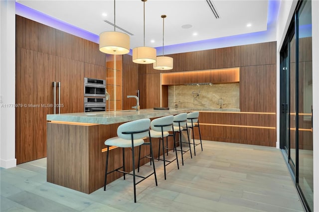 kitchen featuring modern cabinets, brown cabinetry, decorative backsplash, a sink, and stainless steel double oven