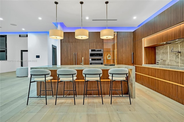 kitchen featuring double oven, light wood-style floors, modern cabinets, and backsplash