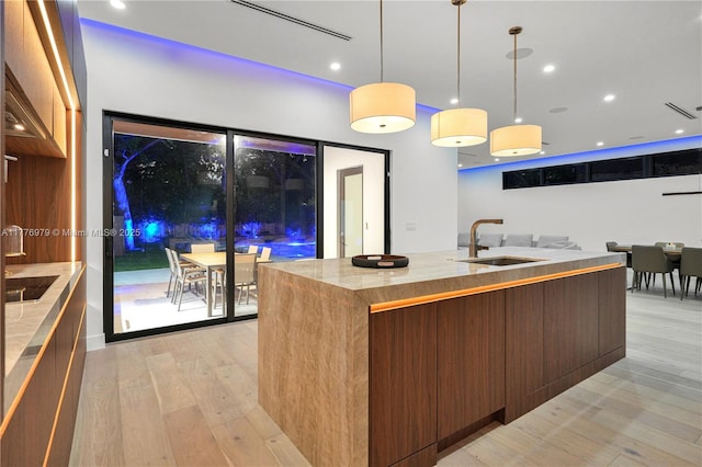 kitchen with a kitchen island with sink, light wood-type flooring, modern cabinets, and a sink