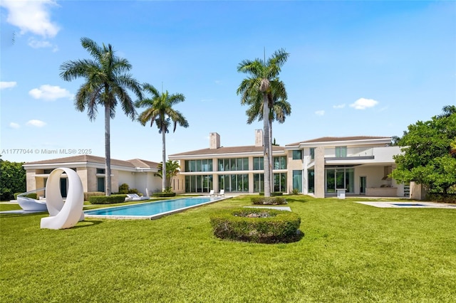 back of house featuring an outdoor pool, a lawn, and stucco siding
