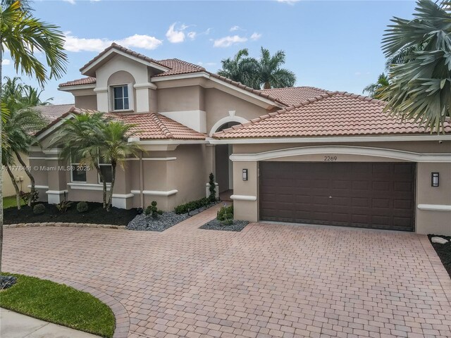 2269 Quail Roost Dr, Weston, FL 33327 - mediterranean / spanish home with stucco siding, a garage, decorative driveway, and a tiled roof