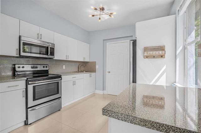 kitchen with a sink, a chandelier, white cabinetry, stainless steel appliances, and decorative backsplash