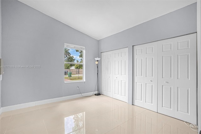 unfurnished bedroom with tile patterned floors, baseboards, two closets, and lofted ceiling