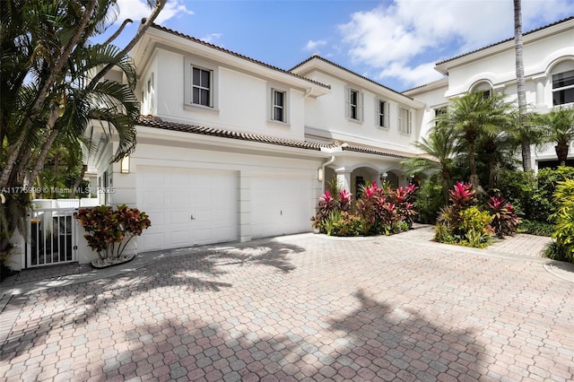 view of front of home featuring an attached garage, a tile roof, stucco siding, and decorative driveway