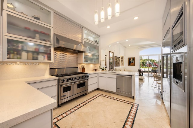 kitchen featuring appliances with stainless steel finishes, ventilation hood, arched walkways, a peninsula, and backsplash
