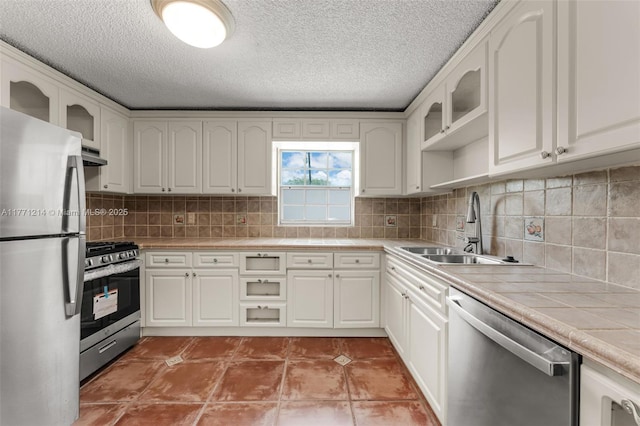 kitchen with a sink, tile counters, white cabinets, and stainless steel appliances