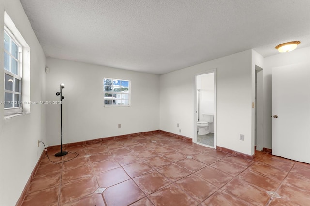 unfurnished bedroom featuring a textured ceiling, light tile patterned flooring, baseboards, and ensuite bath