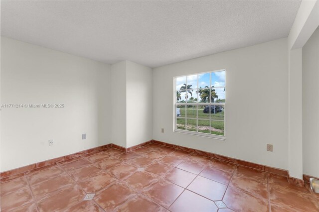 tiled spare room with a textured ceiling and baseboards