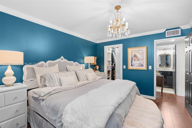 bedroom featuring an inviting chandelier, wood finished floors, visible vents, ornamental molding, and a walk in closet