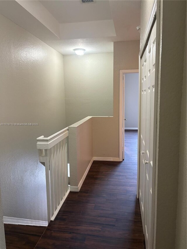 corridor featuring dark wood finished floors, visible vents, an upstairs landing, a textured wall, and baseboards