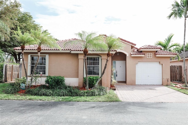 mediterranean / spanish-style house with a tile roof, stucco siding, decorative driveway, an attached garage, and fence