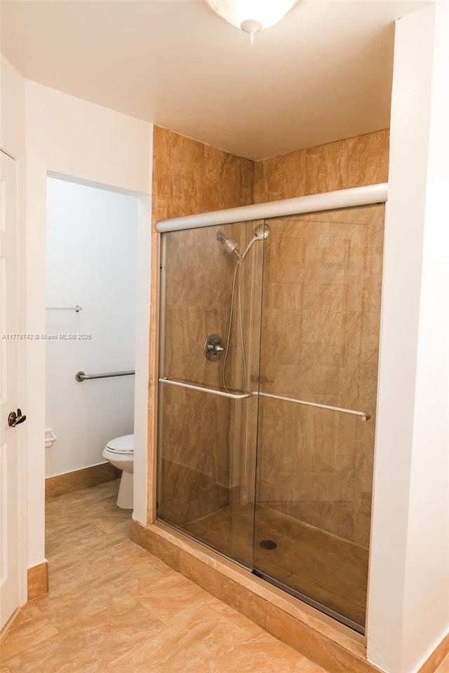 full bath featuring toilet, a stall shower, and baseboards