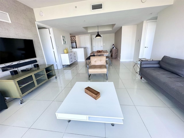living room featuring a tray ceiling, light tile patterned floors, baseboards, and visible vents