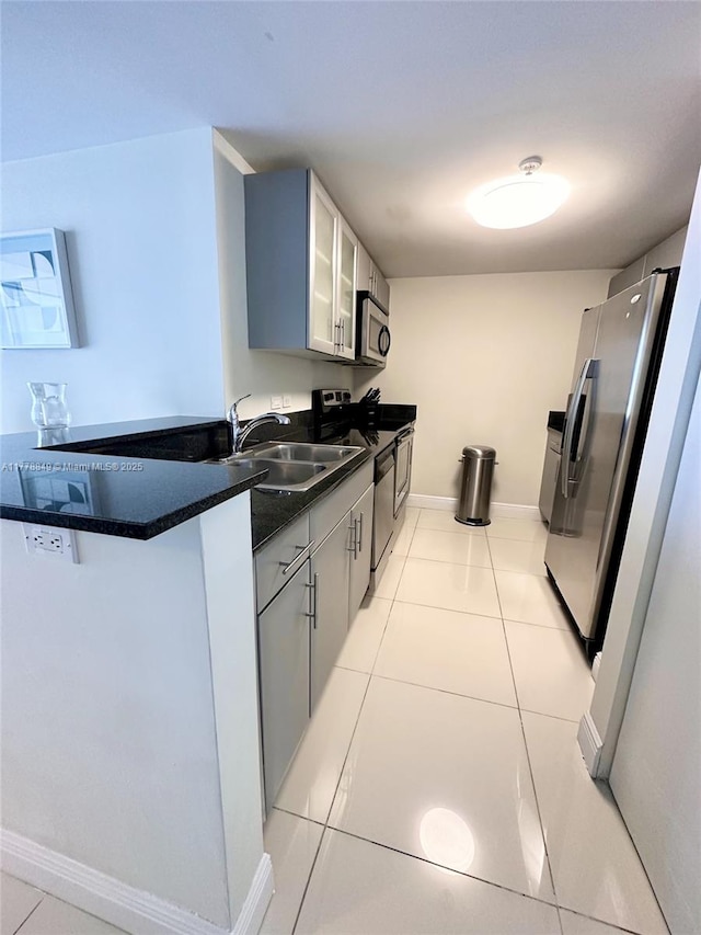 kitchen featuring glass insert cabinets, light tile patterned flooring, a sink, dark countertops, and stainless steel appliances
