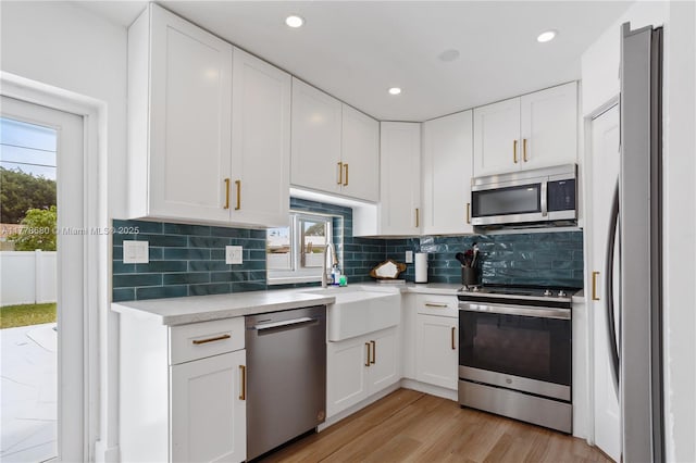 kitchen with a sink, backsplash, light countertops, white cabinets, and appliances with stainless steel finishes