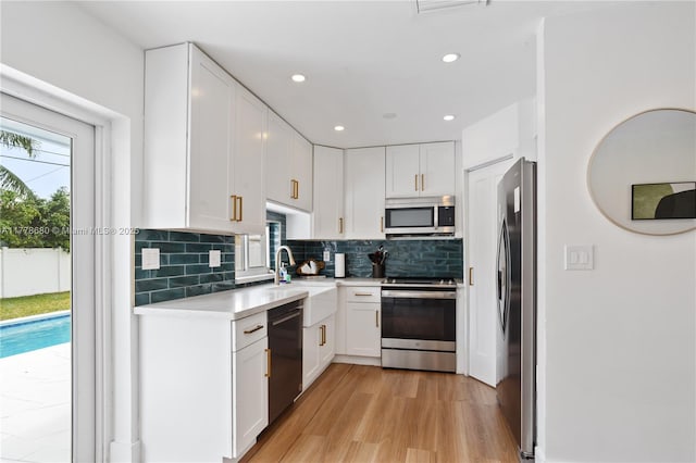 kitchen with a sink, stainless steel appliances, tasteful backsplash, light wood-type flooring, and light countertops
