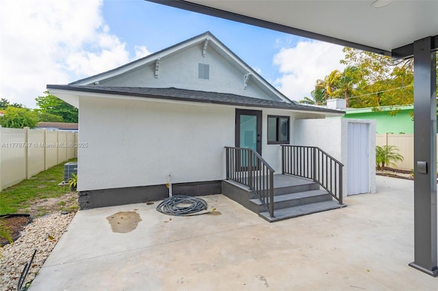 view of front of property featuring a patio area, stucco siding, fence, and a shingled roof