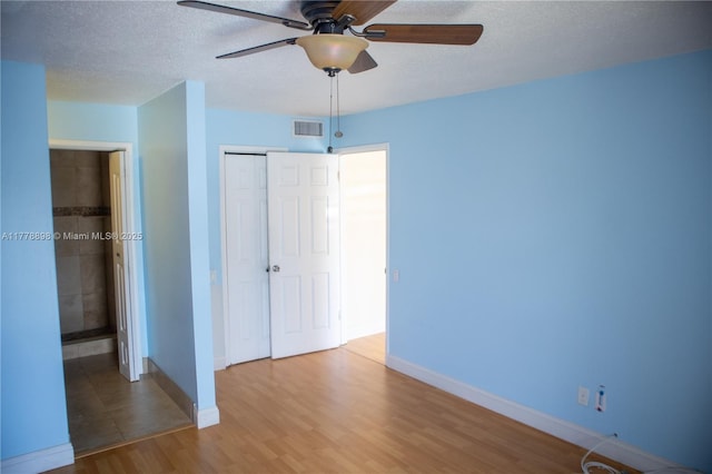 unfurnished bedroom with a textured ceiling, a closet, visible vents, wood finished floors, and baseboards