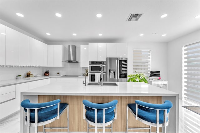 kitchen featuring visible vents, wall chimney exhaust hood, modern cabinets, a sink, and stainless steel appliances