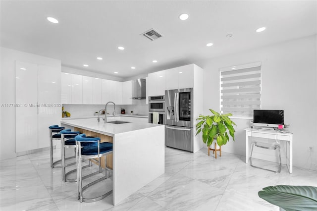kitchen with wall chimney exhaust hood, modern cabinets, visible vents, a sink, and stainless steel appliances