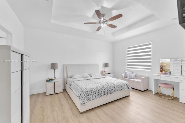 bedroom featuring light wood-style floors, a tray ceiling, baseboards, and ceiling fan