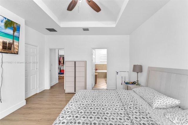 bedroom featuring a raised ceiling, light wood-type flooring, baseboards, and visible vents