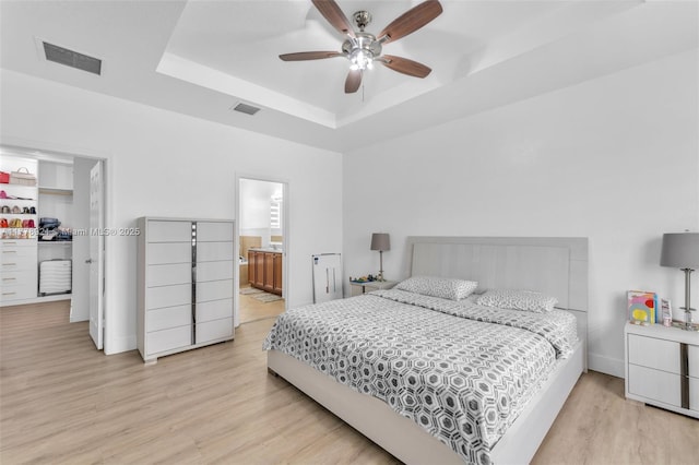 bedroom with visible vents, light wood-type flooring, and a raised ceiling