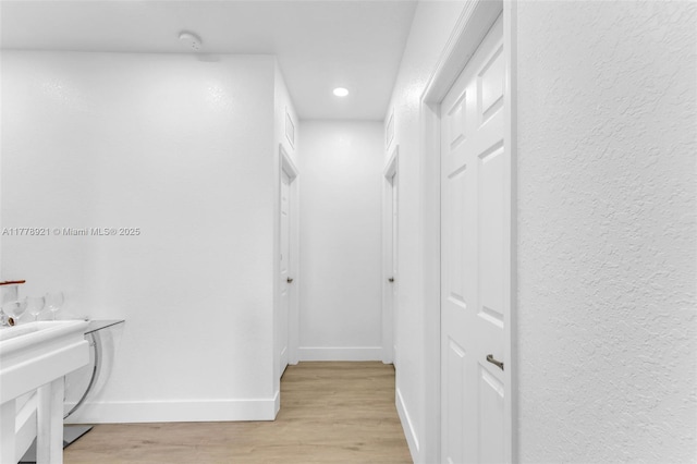 hall featuring baseboards, light wood finished floors, and recessed lighting