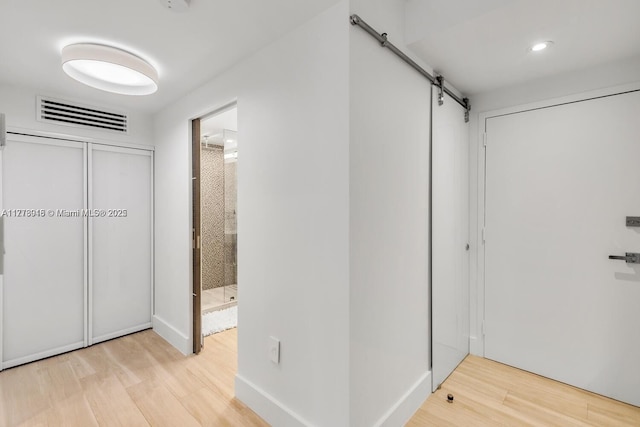 corridor with visible vents, light wood-style flooring, and a barn door