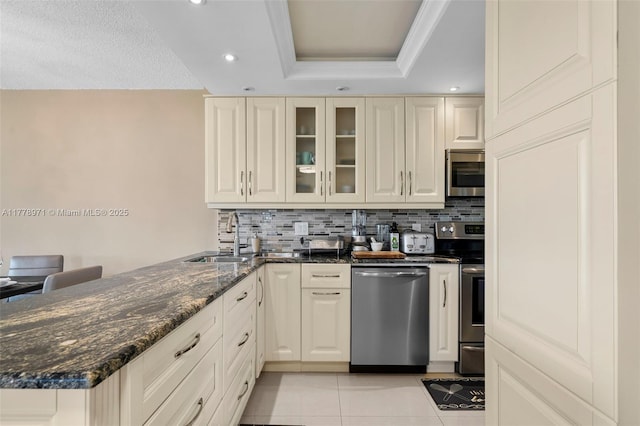 kitchen featuring light tile patterned flooring, a raised ceiling, backsplash, a peninsula, and appliances with stainless steel finishes