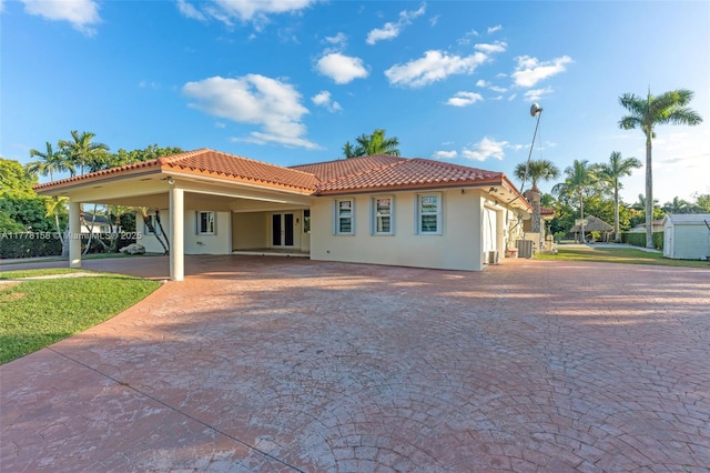 back of house featuring a tiled roof, a carport, driveway, central AC, and stucco siding
