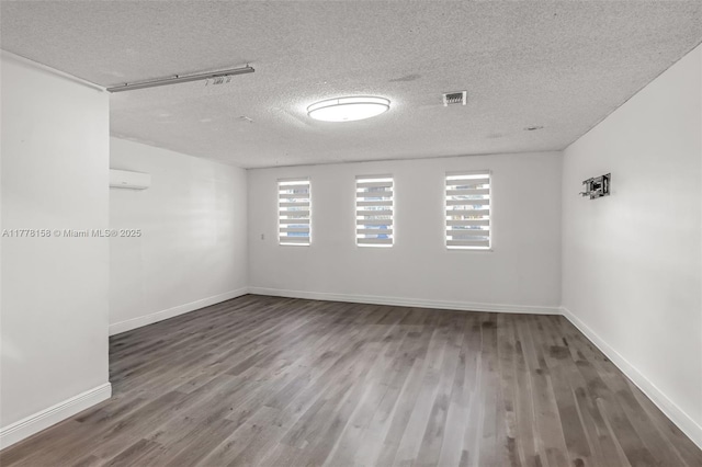 spare room with a wall mounted air conditioner, baseboards, wood finished floors, and a textured ceiling