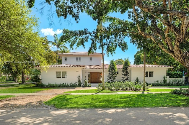 mediterranean / spanish home featuring a tile roof, a front lawn, and stucco siding