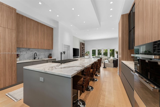 kitchen featuring a breakfast bar, open floor plan, backsplash, modern cabinets, and light wood finished floors