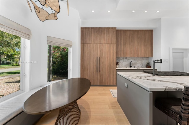 kitchen featuring modern cabinets, light stone counters, a sink, brown cabinets, and backsplash