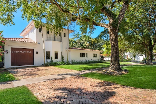 mediterranean / spanish-style house with a tiled roof, decorative driveway, a front lawn, a balcony, and an attached garage