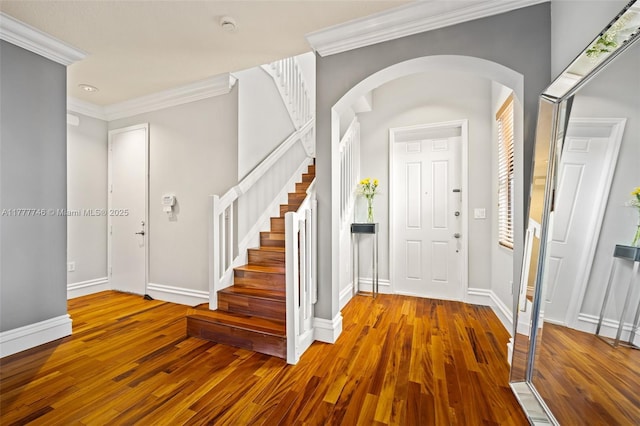 foyer featuring crown molding, arched walkways, wood finished floors, stairs, and baseboards