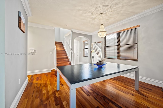 unfurnished dining area featuring arched walkways, wood finished floors, ornamental molding, and stairway
