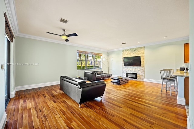 living area with crown molding, wood finished floors, a stone fireplace, and visible vents