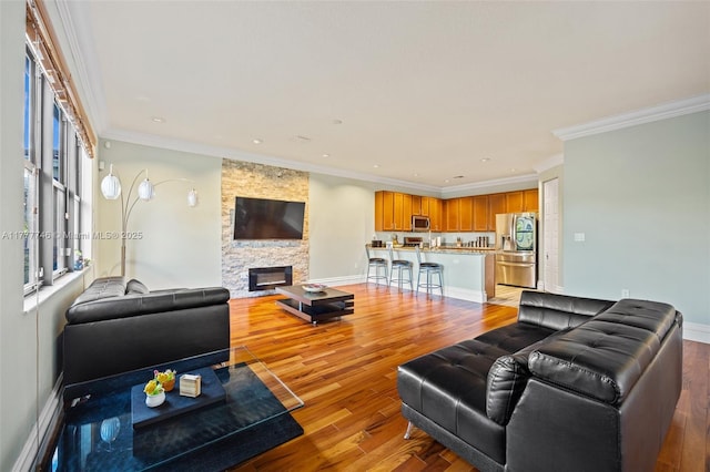 living room featuring light wood finished floors, ornamental molding, and a stone fireplace
