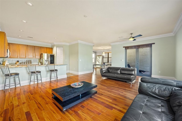 living room featuring baseboards, ornamental molding, recessed lighting, ceiling fan, and light wood finished floors