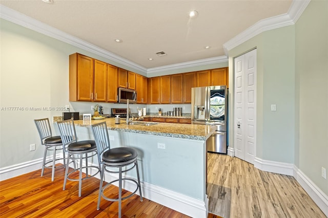 kitchen with a sink, a peninsula, stainless steel appliances, light wood-style flooring, and light stone counters