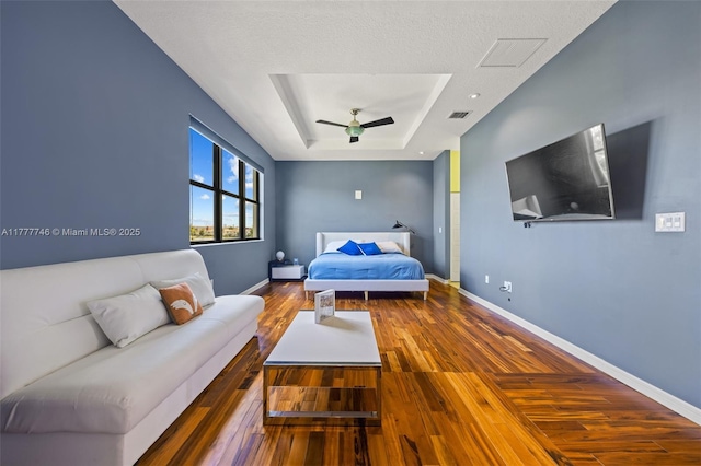 bedroom featuring baseboards, a raised ceiling, visible vents, hardwood / wood-style floors, and ceiling fan