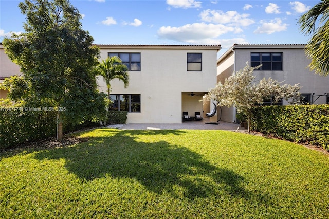 rear view of property with a yard, a tiled roof, a ceiling fan, a patio, and stucco siding