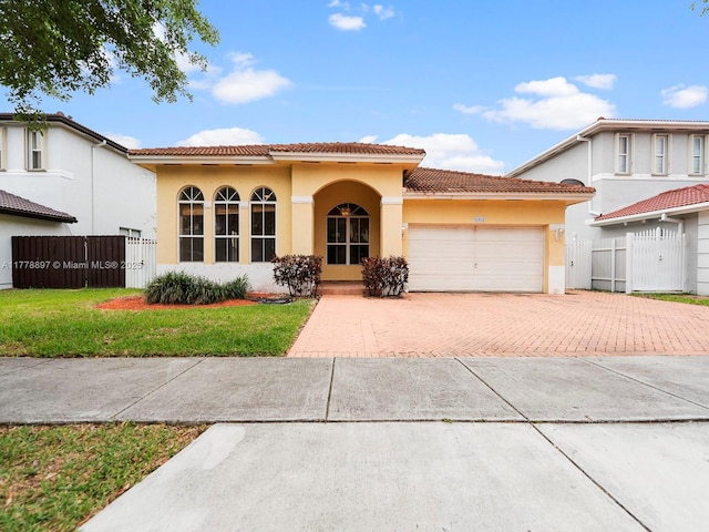 mediterranean / spanish home featuring a tile roof, fence, decorative driveway, and stucco siding