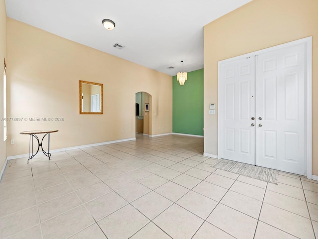 interior space featuring arched walkways, light tile patterned floors, visible vents, and baseboards