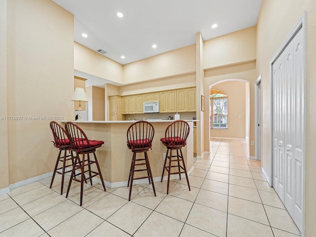 kitchen with white microwave, a kitchen breakfast bar, arched walkways, and light brown cabinets
