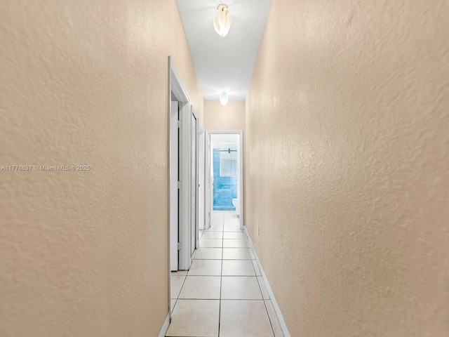 corridor with a textured wall, baseboards, and light tile patterned flooring